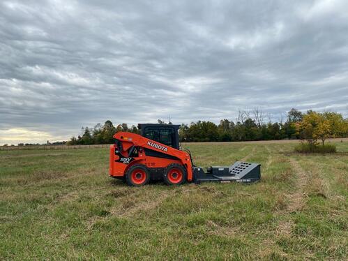 Skid-steer equipped with brush mower in overgrown field.